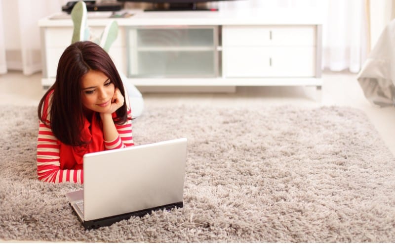 jeune femme face à son ordinateur , allongé sur un tapis à poils long